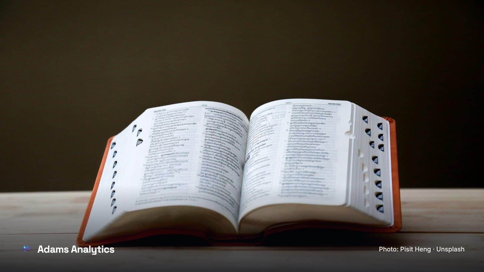 A thick dictionary with thumb-index tabs lying open on a wooden table