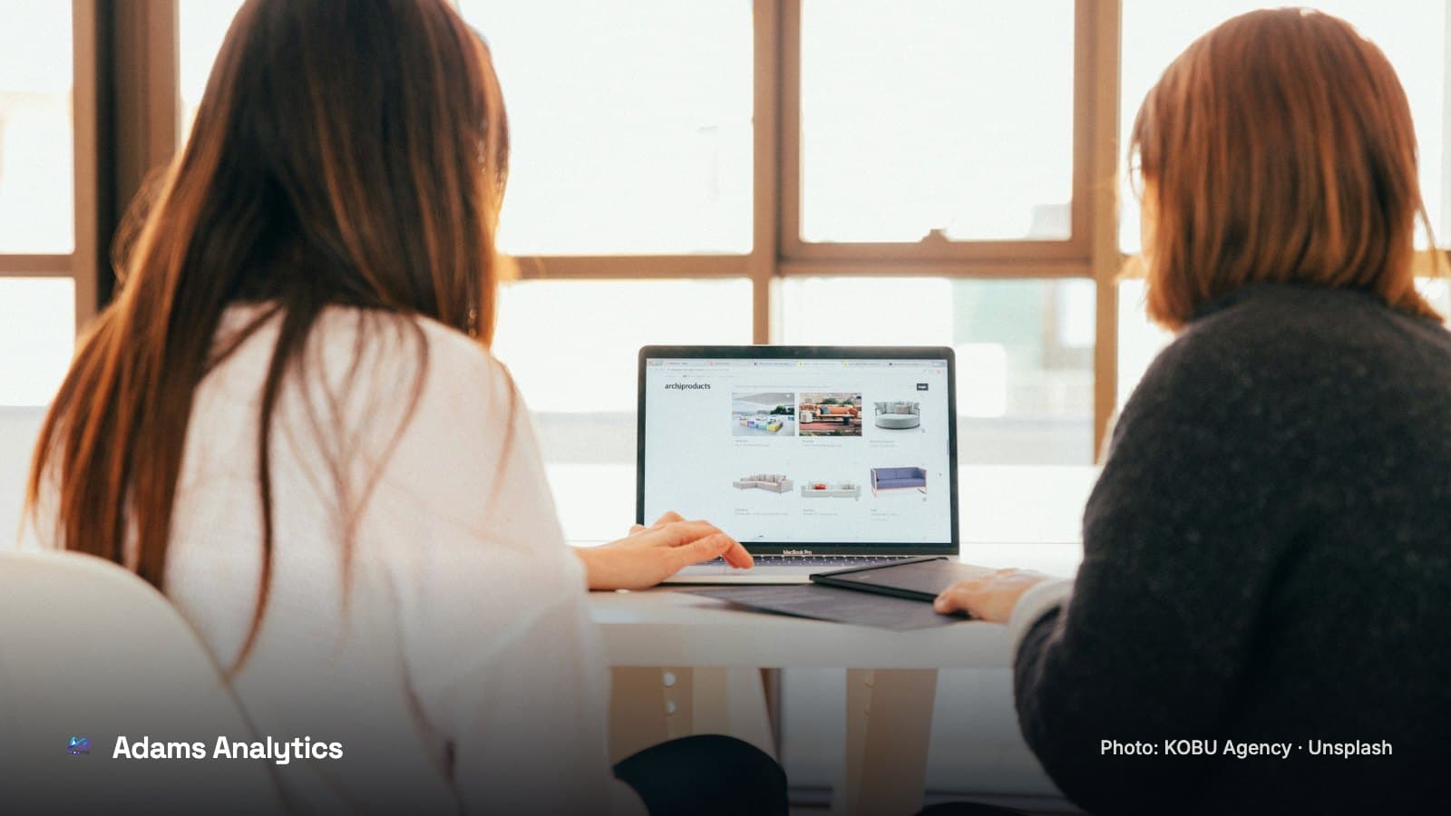 Two women looking at a laptop together at a table in a bright office