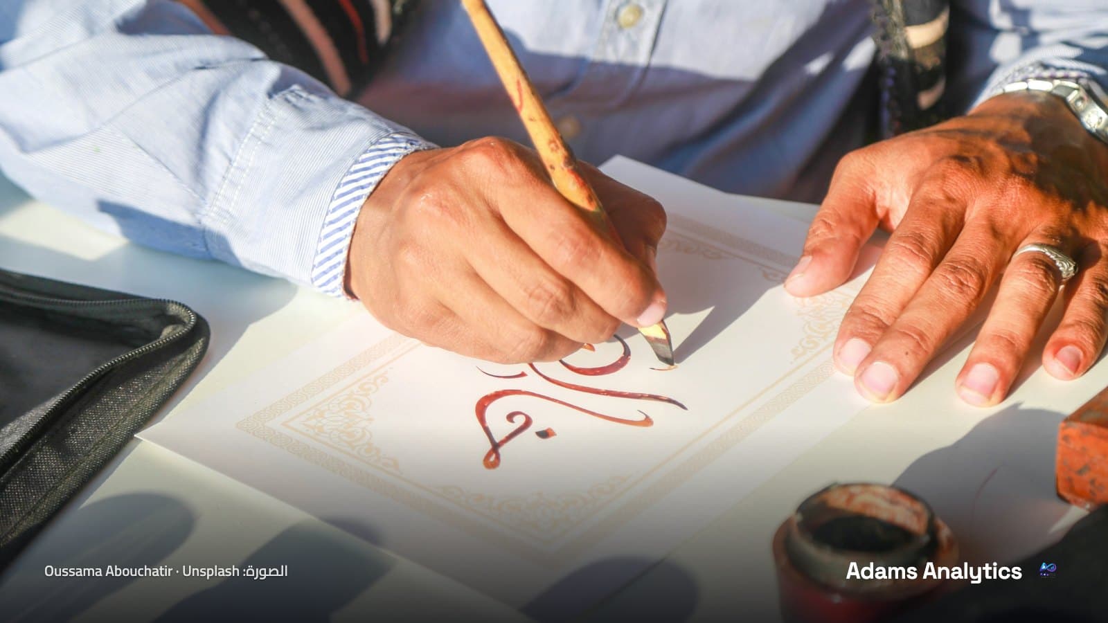 خطاط يكتب حروفًا عربية بحبر أحمر داكن بقلم من القصب