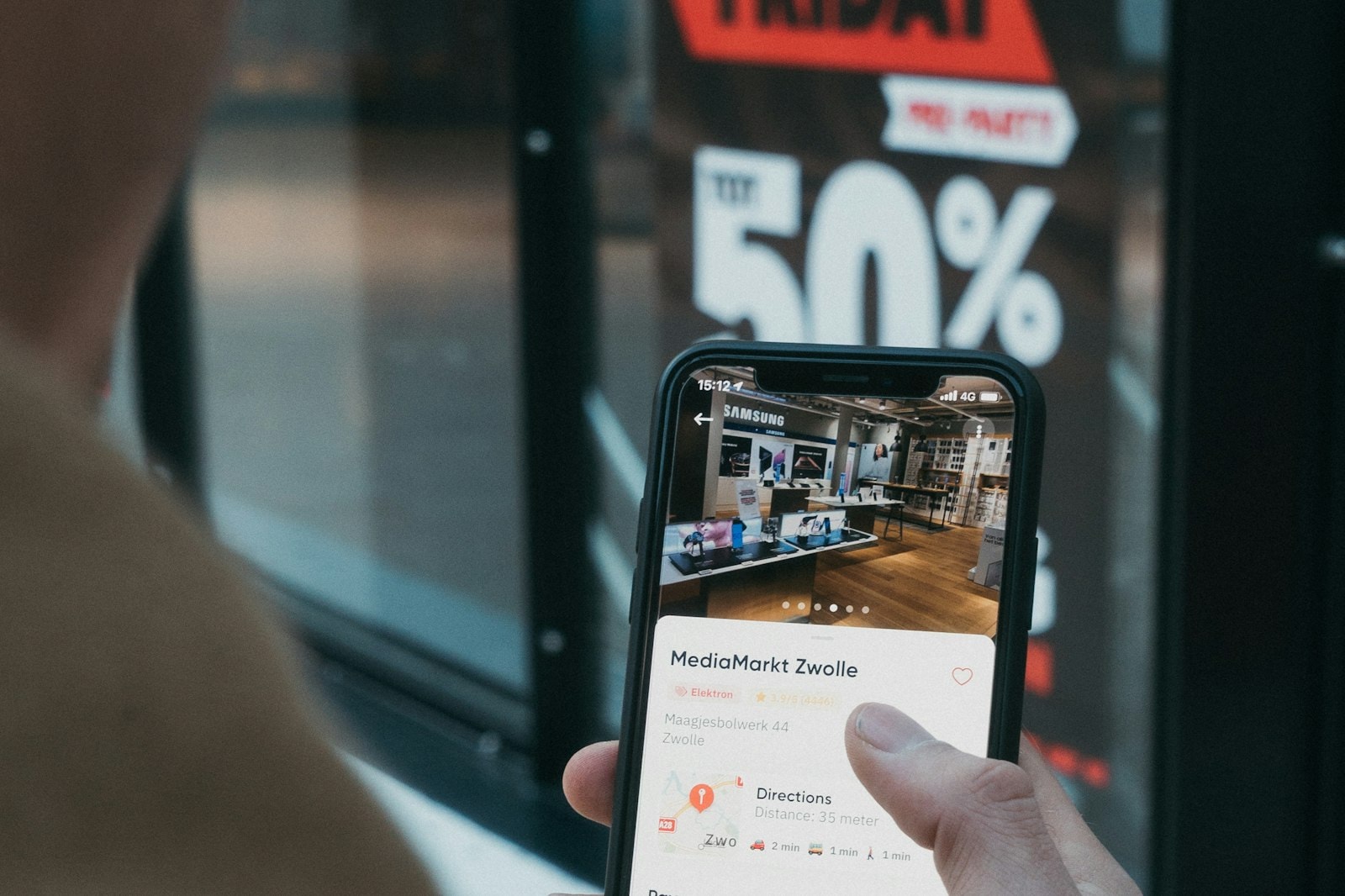 A phone showing an online store in front of a shop window with a sale sign