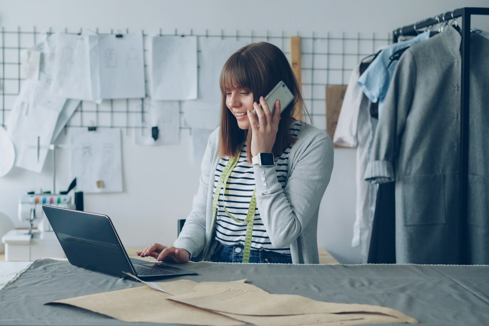 A young founder on the phone while working on a laptop in a clothing studio