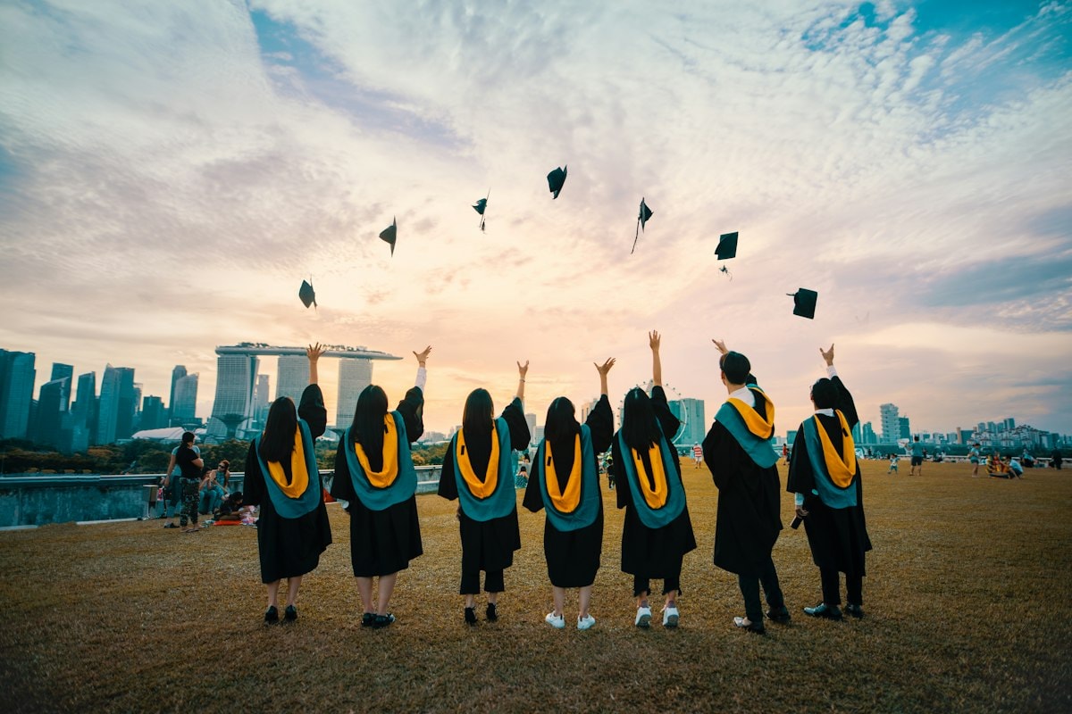 Graduates in black gowns throwing their caps in the air at sunset
