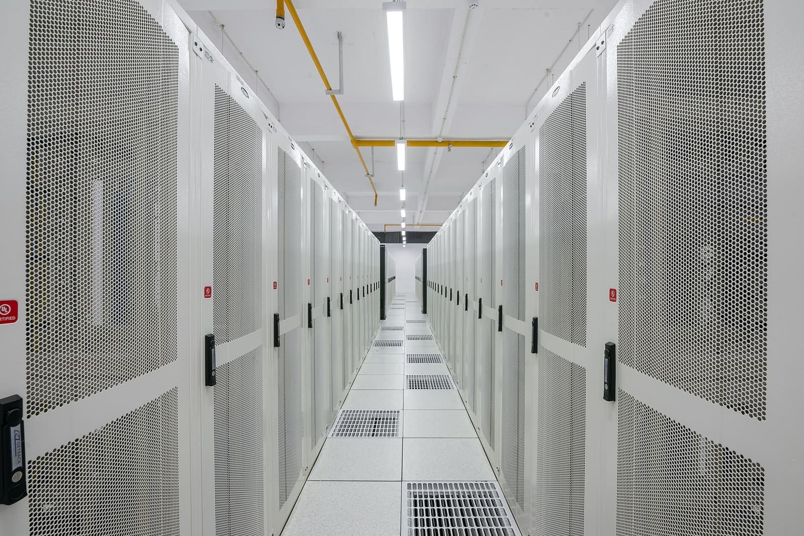 A long, bright corridor between rows of white server cabinets in a data center