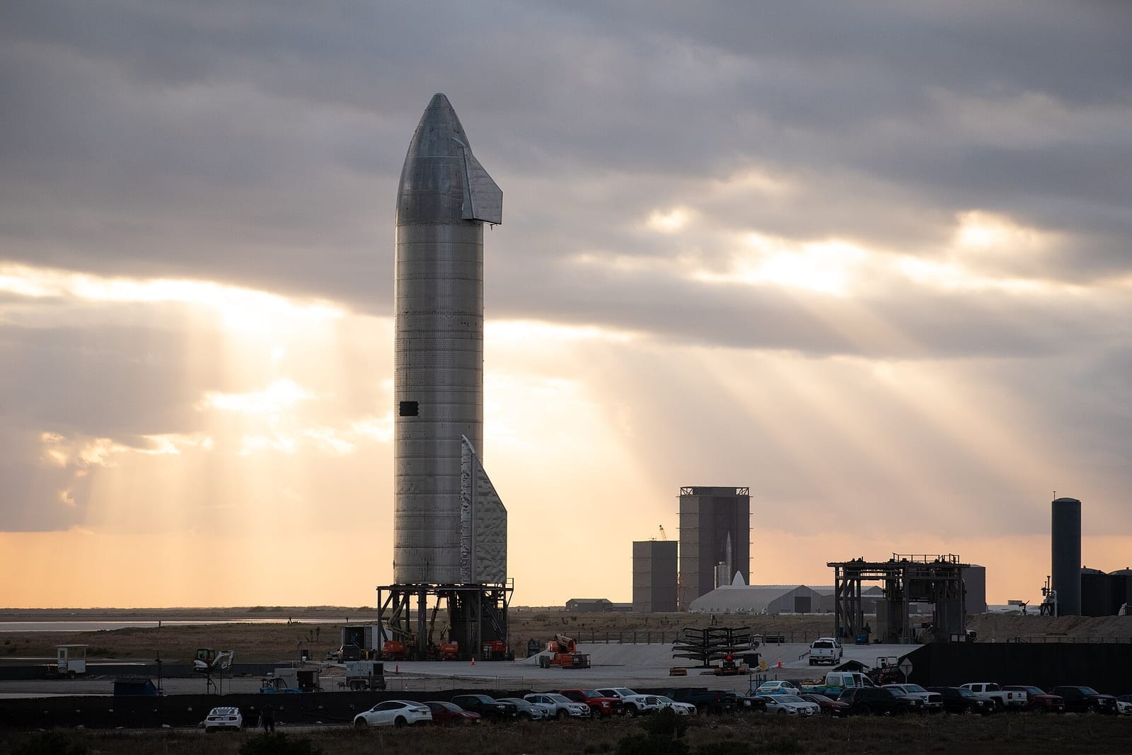 A SpaceX Starship rocket on its launch site in Texas, with sun rays breaking through clouds