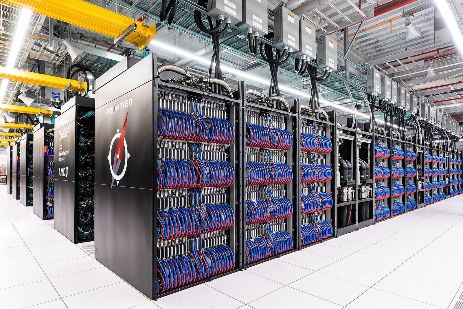 Rows of supercomputer cabinets full of blue cables in a bright data hall