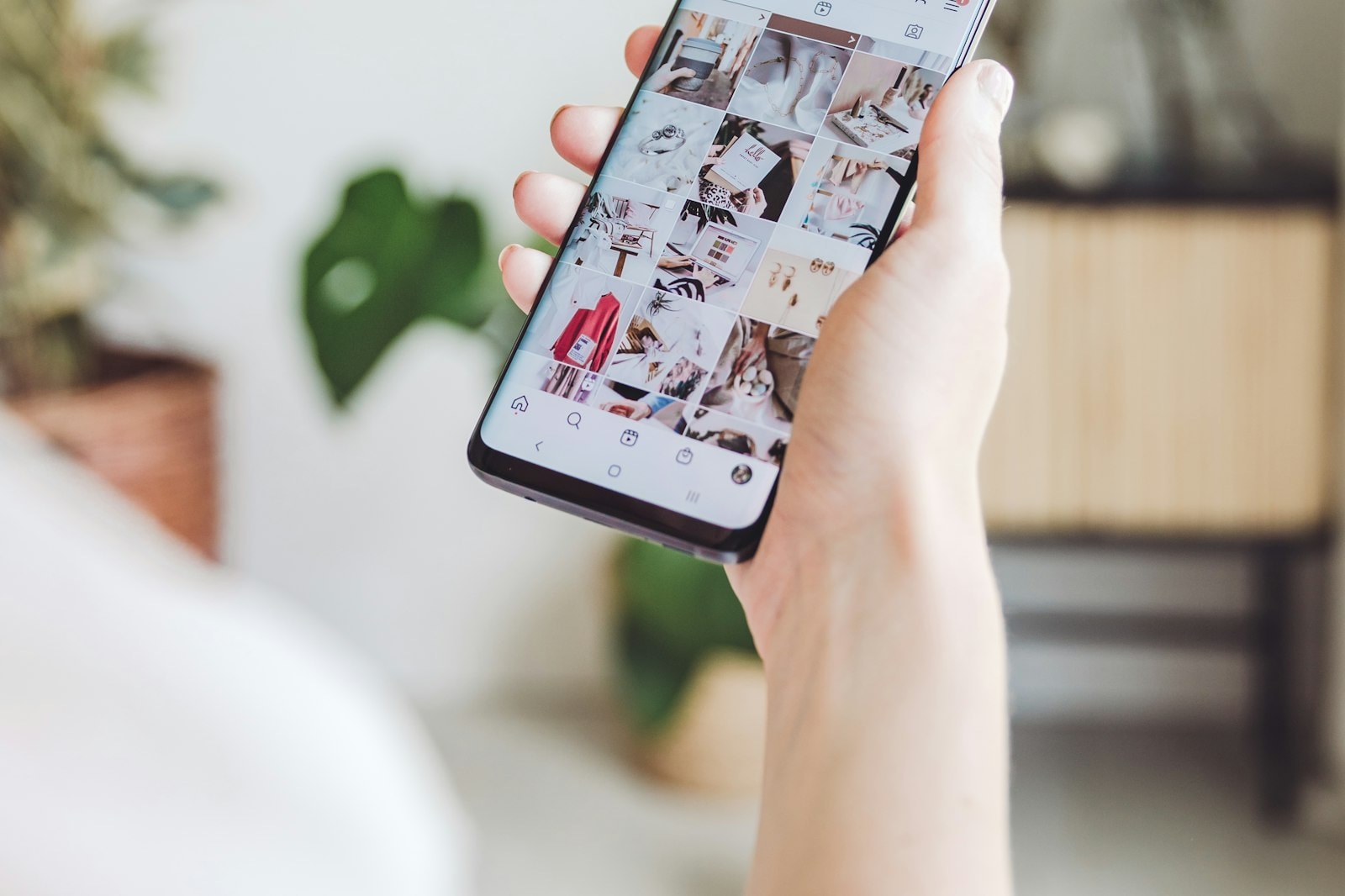 A hand holding a phone with a social feed full of images