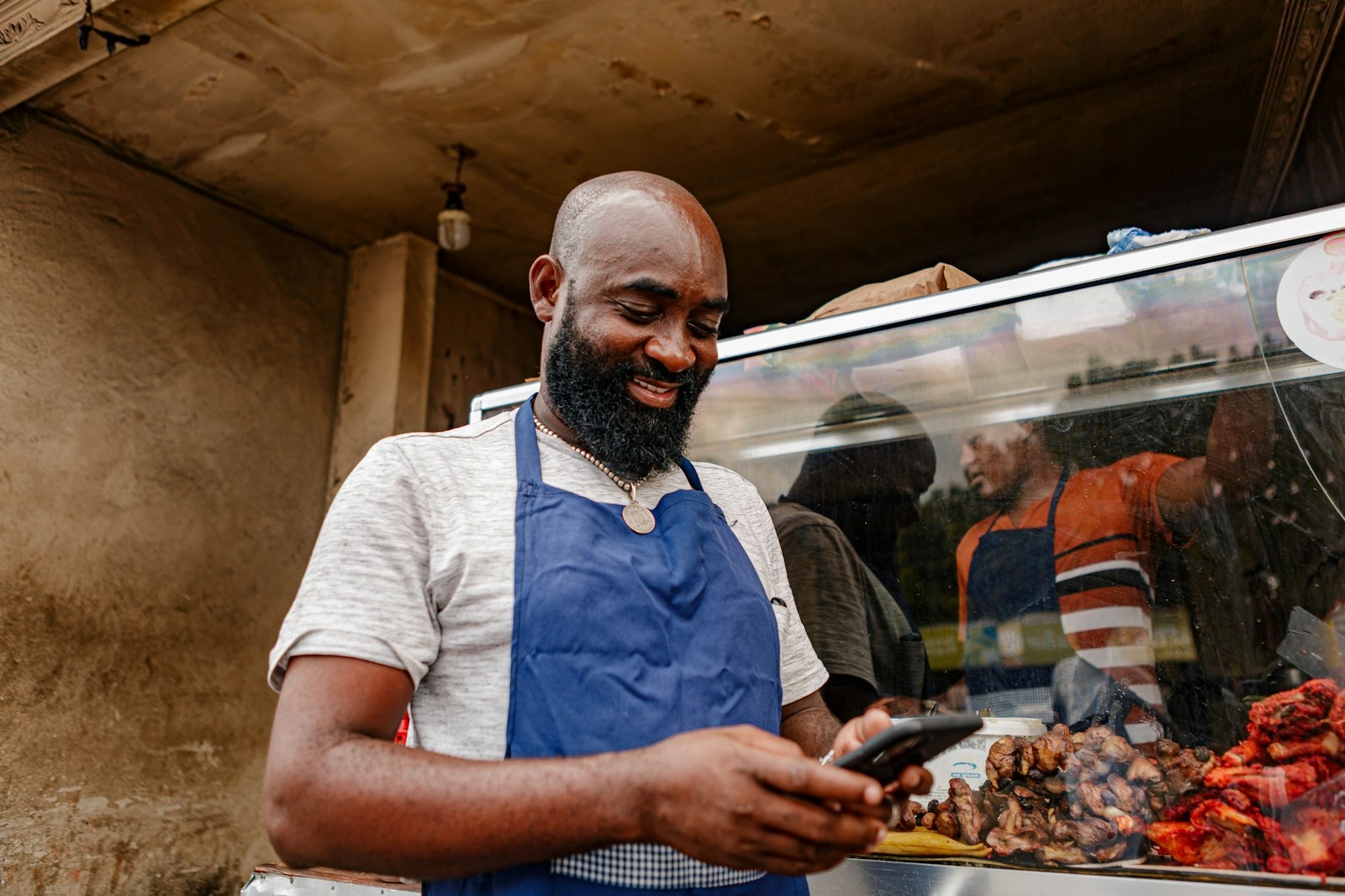 A shop owner in an apron smiling at his phone