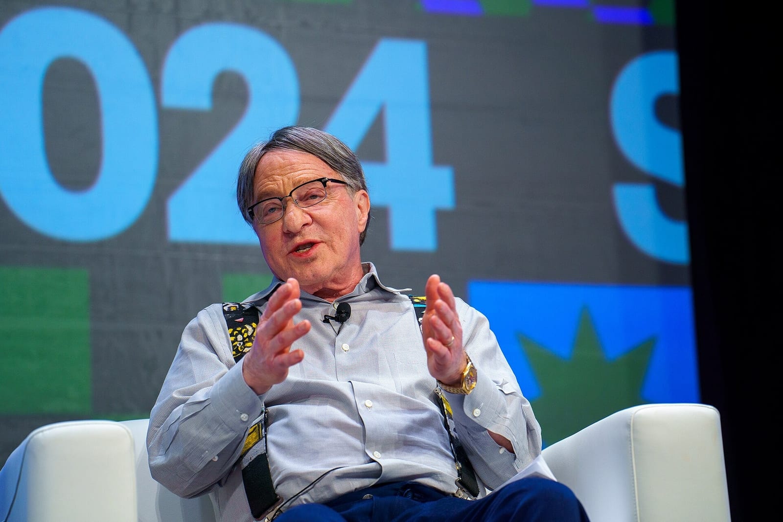 Ray Kurzweil in glasses speaking on stage, with a large 2024 sign behind him