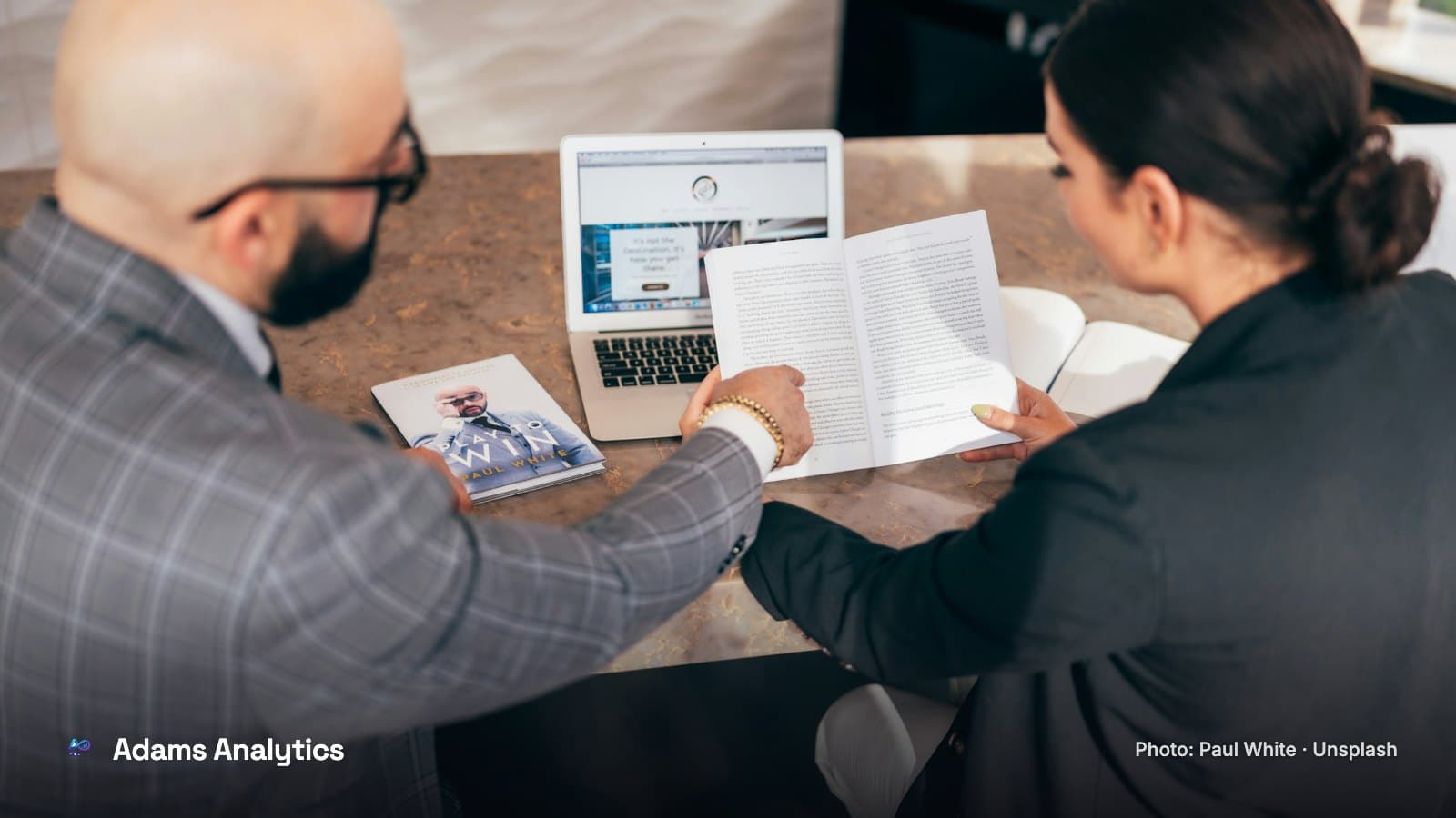 A man and a woman reviewing printed pages beside an open laptop at a meeting table