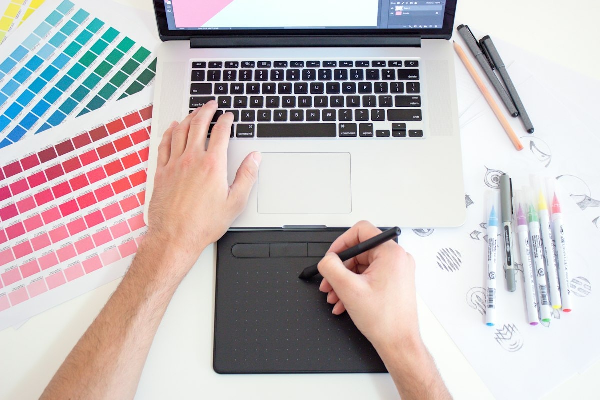 Hands using a digital drawing tablet next to a laptop and color swatches