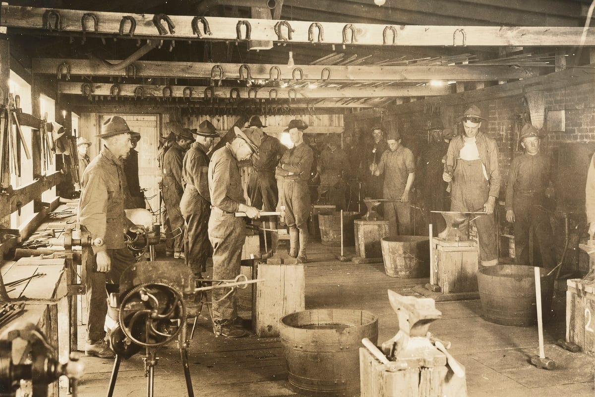 Soldiers learning horseshoeing and blacksmithing in a workshop in 1918, with horseshoes hanging from the beams