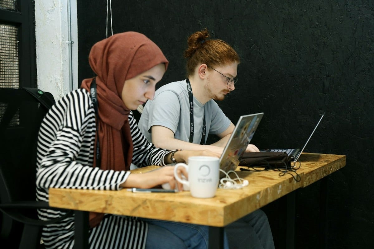Two young developers working on laptops at a wooden table