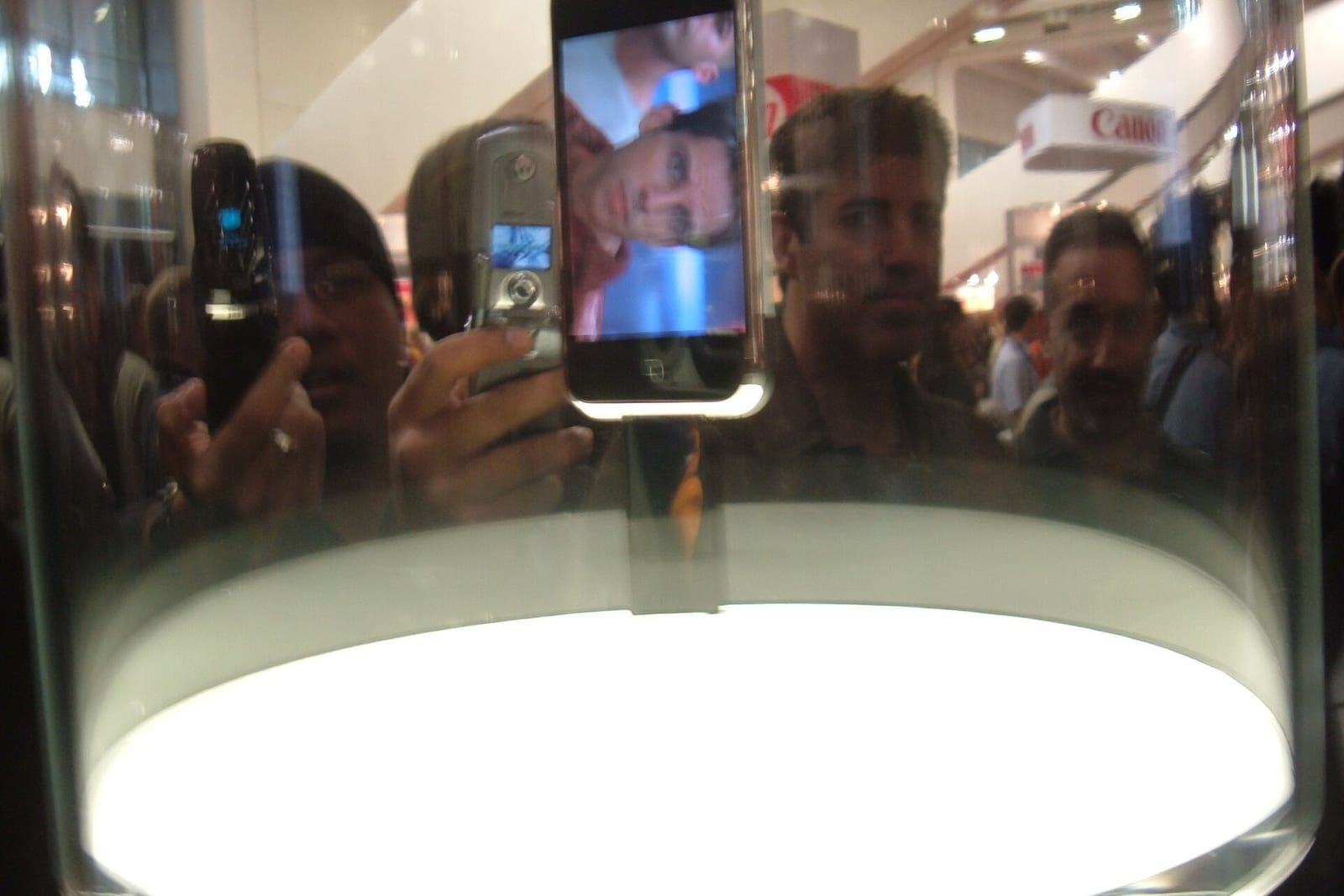 The first iPhone on display in a glass case at Macworld 2007, with a crowd reflected around it