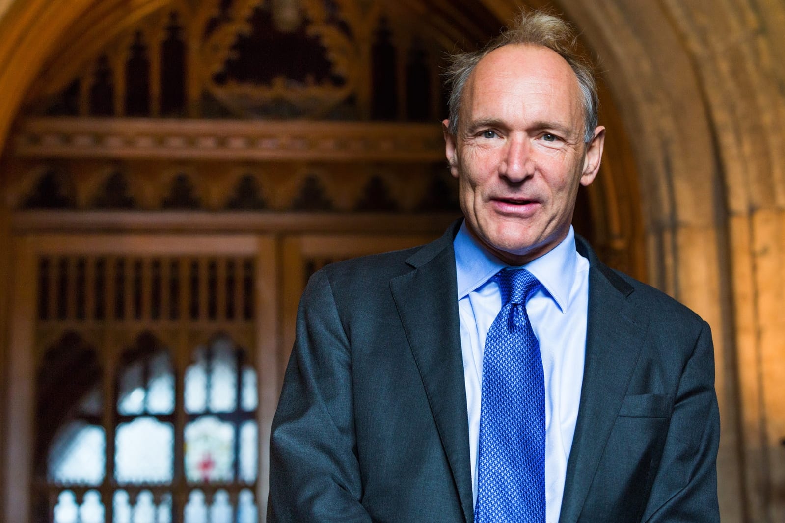 Tim Berners-Lee in a suit and blue tie, smiling, in a wood-panelled hall